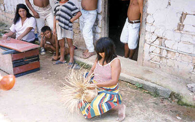 A woman weaving a basket in front of her home